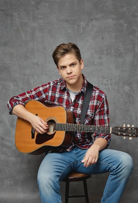 as a 90s indie musician, in a plaid shirt, skinny jeans, with a vintage acoustic guitar, looking introspective, against a traditional yearbook setting