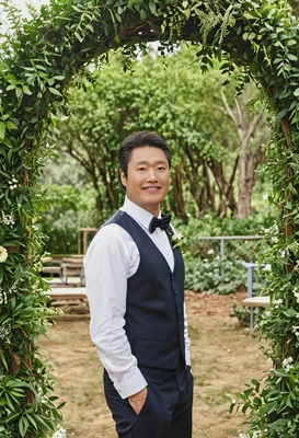 as the groom in an outdoor ceremony surrounded by lush greenery and decorated arch