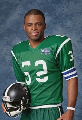 as a 90s football player in a green and white jersey, holding a helmet under one arm, standing against a classic blue yearbook backdrop