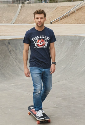 as a man, riding a skateboard down in a skateboard park, wearing a casual t-shirt and jeans