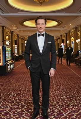 as James Bond from Skyfall, wearing a tailored black tuxedo with a bow tie, confident, standing in a luxurious casino, full body view 