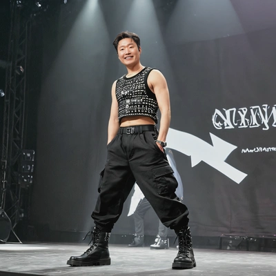 as a K-pop idol, wearing a stylish crop top, cargo pants, and chunky boots, performing an energetic dance routine on a brightly lit stage, mid shot photo