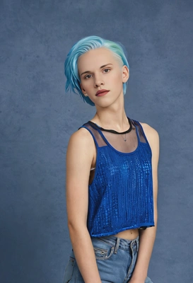 with bright dyed hair, wearing a mesh top over a tank top, standing proudly, classic blue yearbook backdrop 
